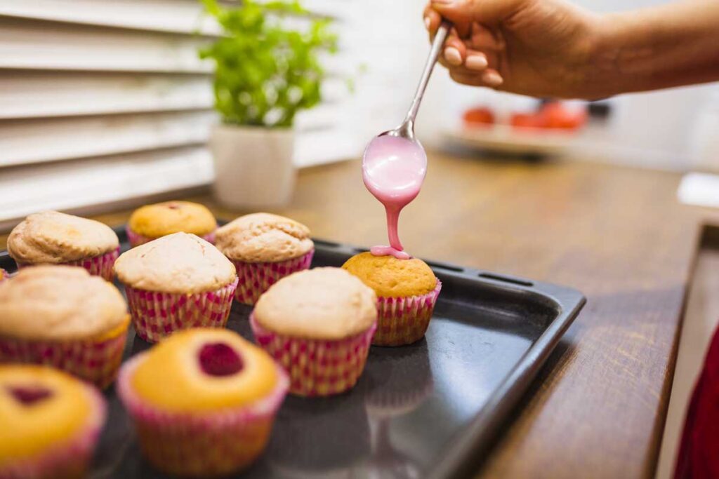 crop hand pouring sauce onto muffins