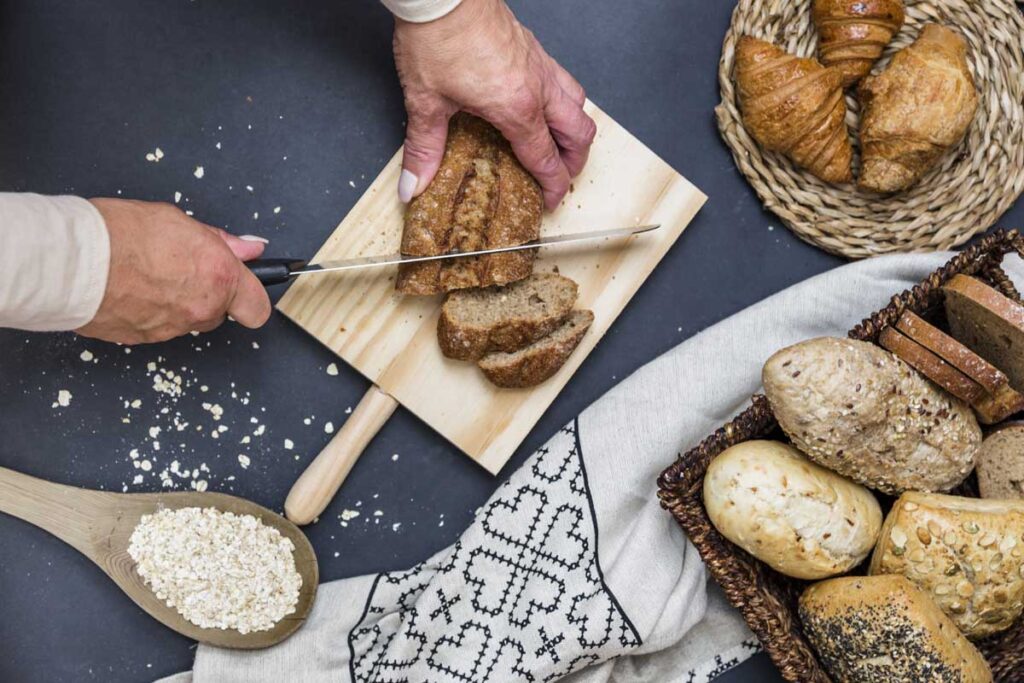 elevated view human hand slicing bread chopping board